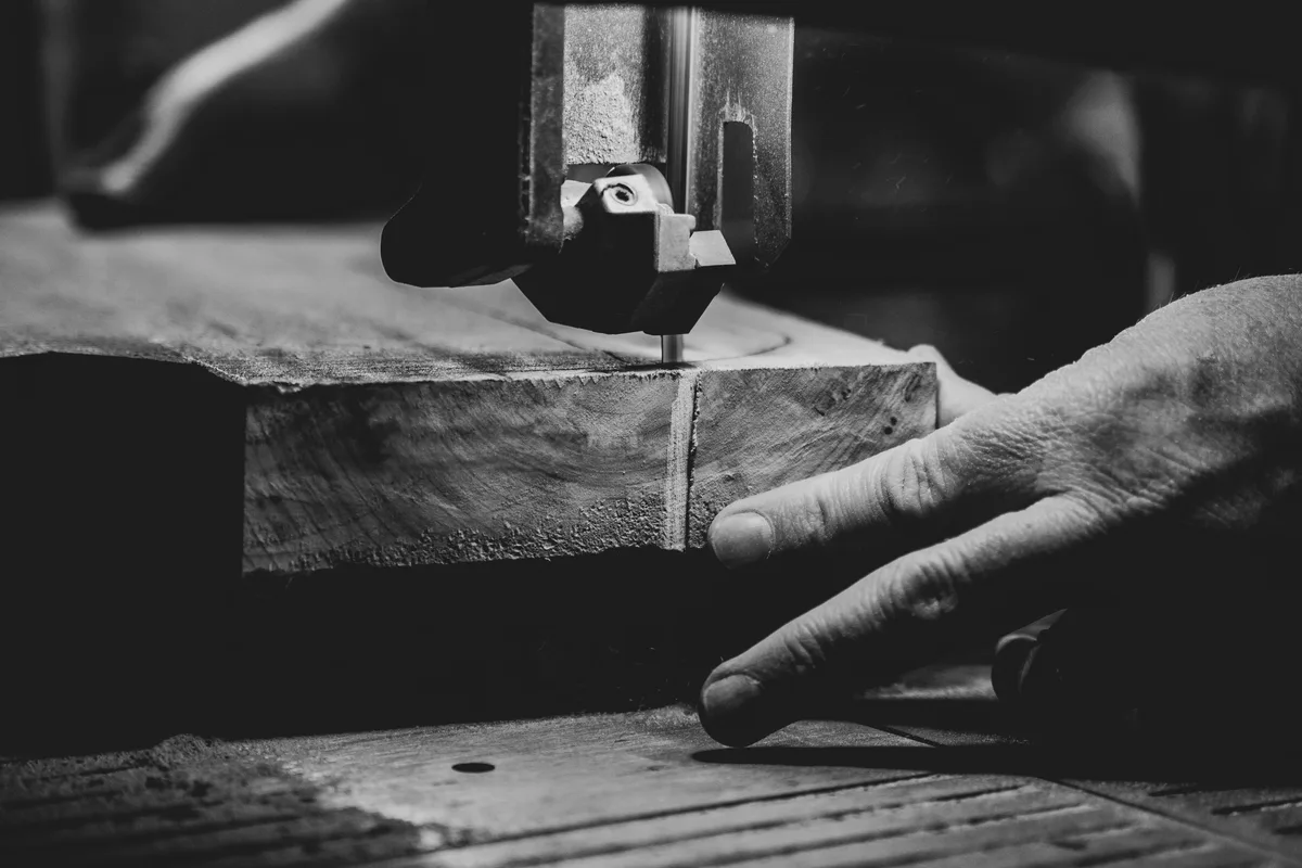 Black-and-white study of hands guiding wood through a bandsaw
